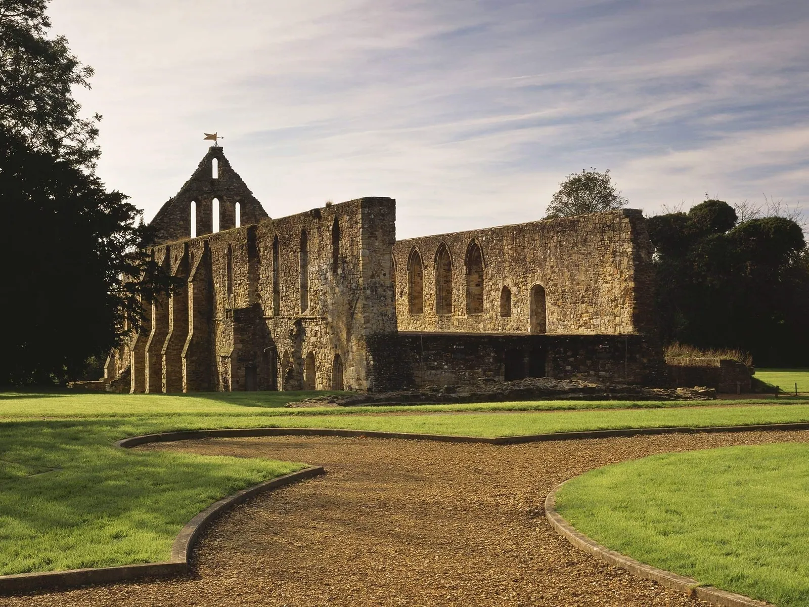 The ruined east range and dormitory of Battle Abbey across the lawn, with a curving gravel path