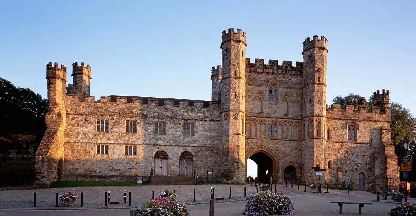 The great gatehouse of Battle Abbey and its battlemented range glowing in evening sunlight