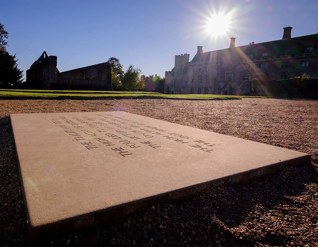 The inscribed stone marking the site of the high altar at Battle Abbey, with the ruins in low sun