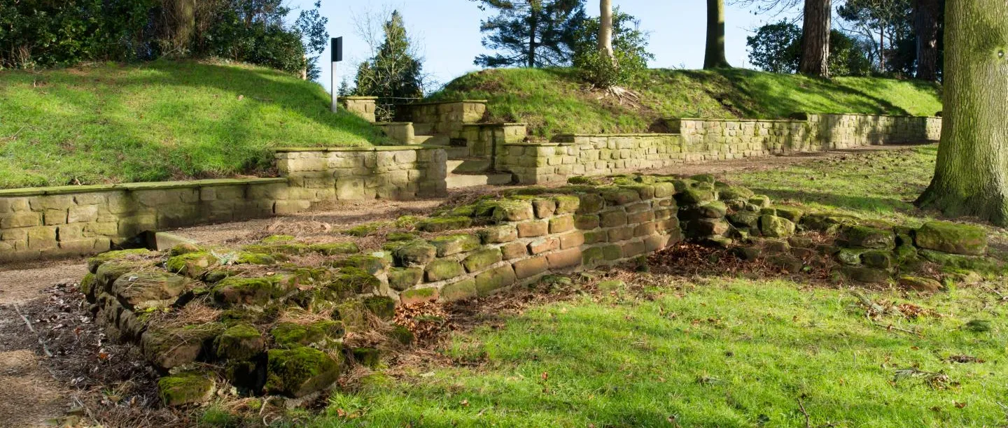 The low sandstone foundations of Aldborough's Roman town wall and tower below grassy banks on a sunny day