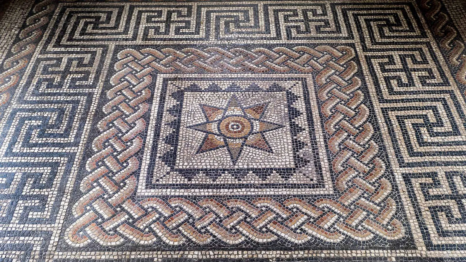 A Roman mosaic floor at Aldborough with an eight-pointed star framed by guilloche plait and a key-pattern border