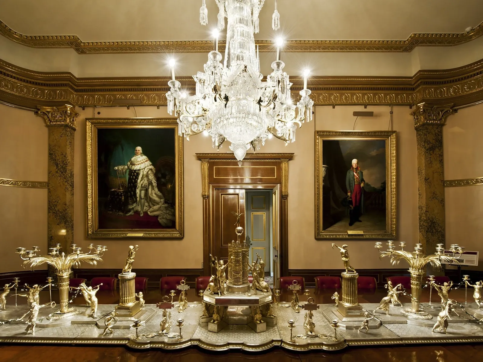 The dining room at Apsley House with its chandelier and gilded silver centrepiece below royal portraits