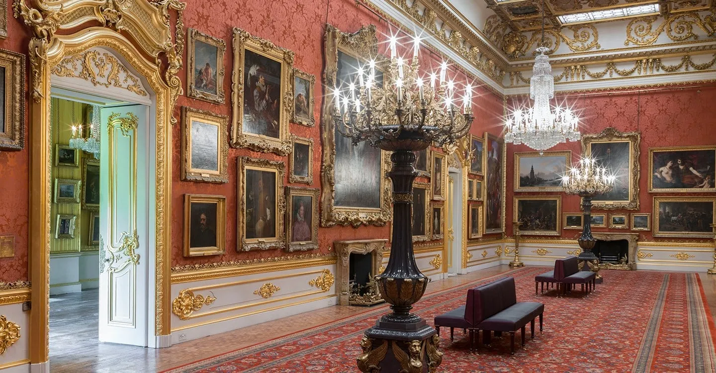 The Waterloo Gallery at Apsley House, hung with paintings under chandeliers, seen from a gilded doorway