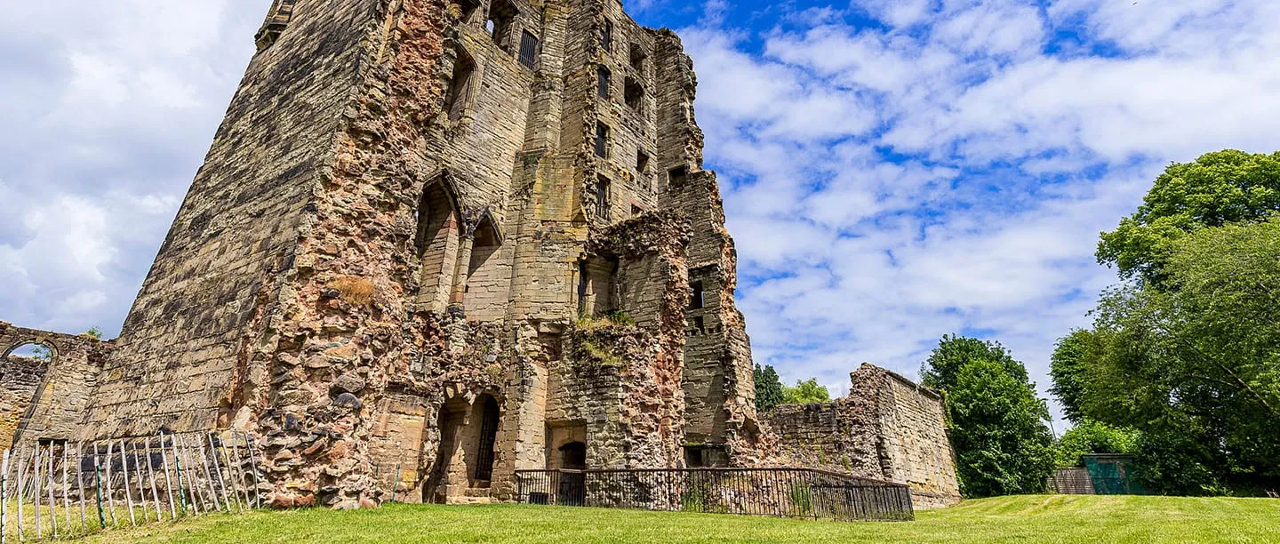 The tall sandstone Hastings Tower of Ashby de la Zouch Castle above a lawn under a summer sky