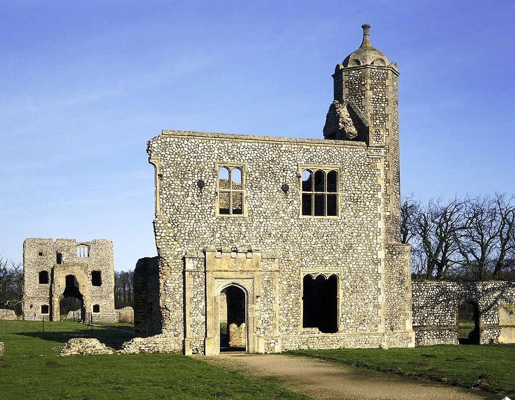 The flint outer gatehouse of Baconsthorpe Castle with its domed octagonal turret and Tudor windows under a deep blue sky