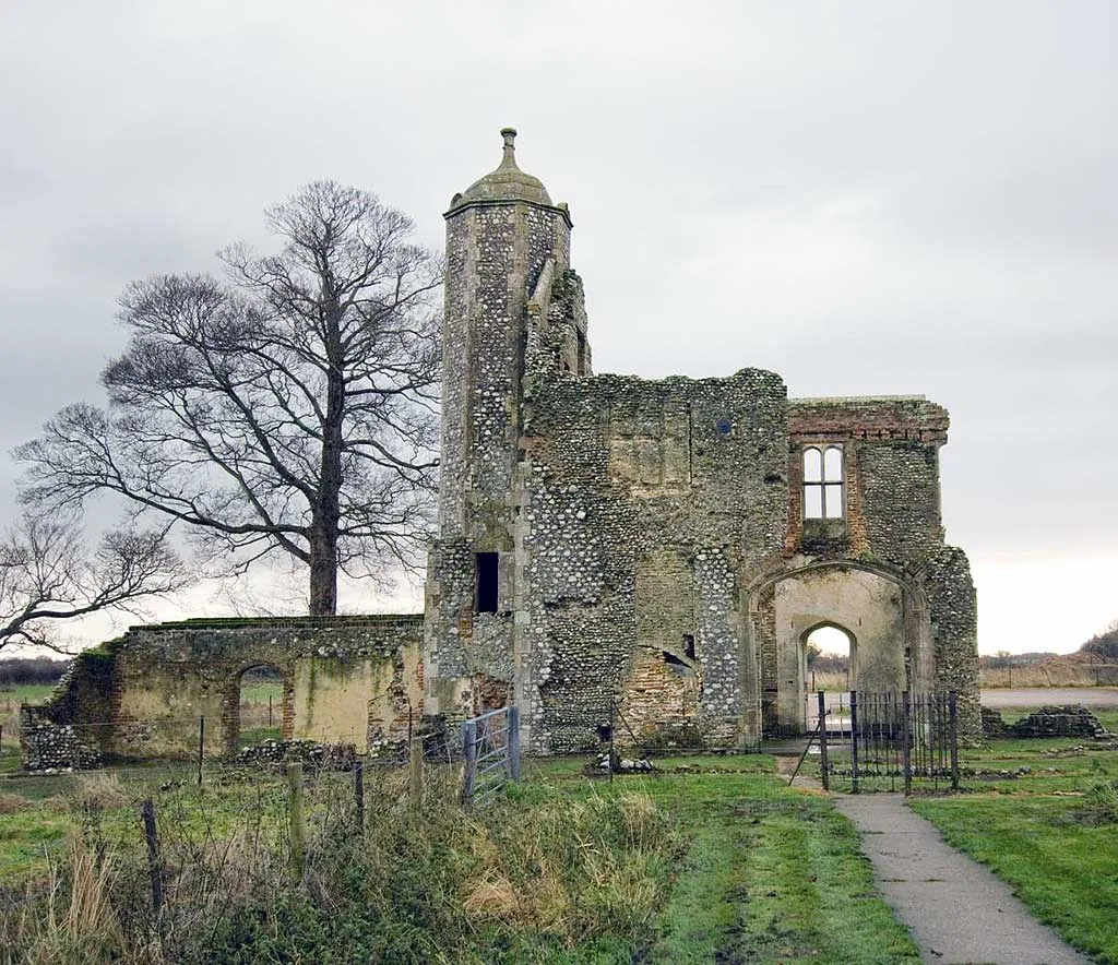 The back of Baconsthorpe Castle's outer gatehouse, with its turret and an archway, beside a bare tree on a grey winter day