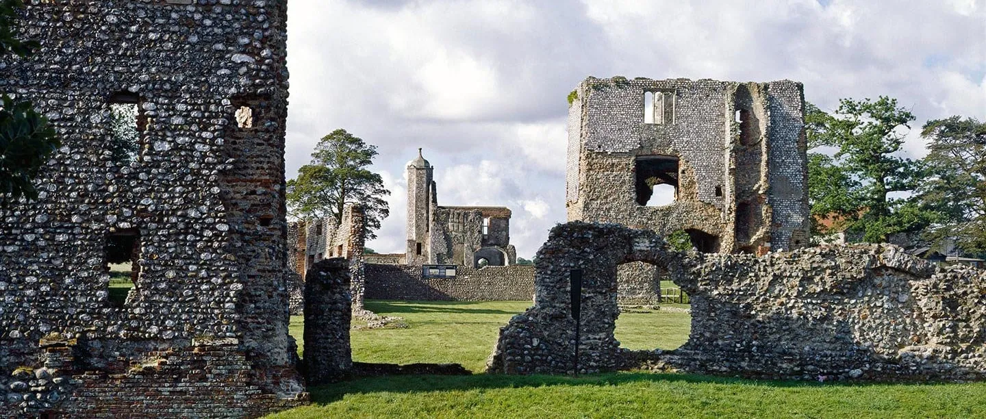 The flint inner gatehouse of Baconsthorpe Castle seen across the courtyard past a ruined wall, with the outer gatehouse turret beyond