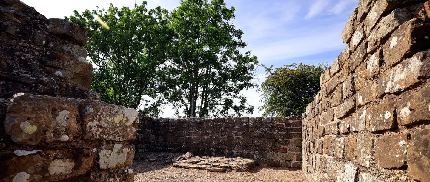 Inside Banks East Turret, with thick sandstone walls around a gravel floor and a stone hearth, beneath trees and a blue sky