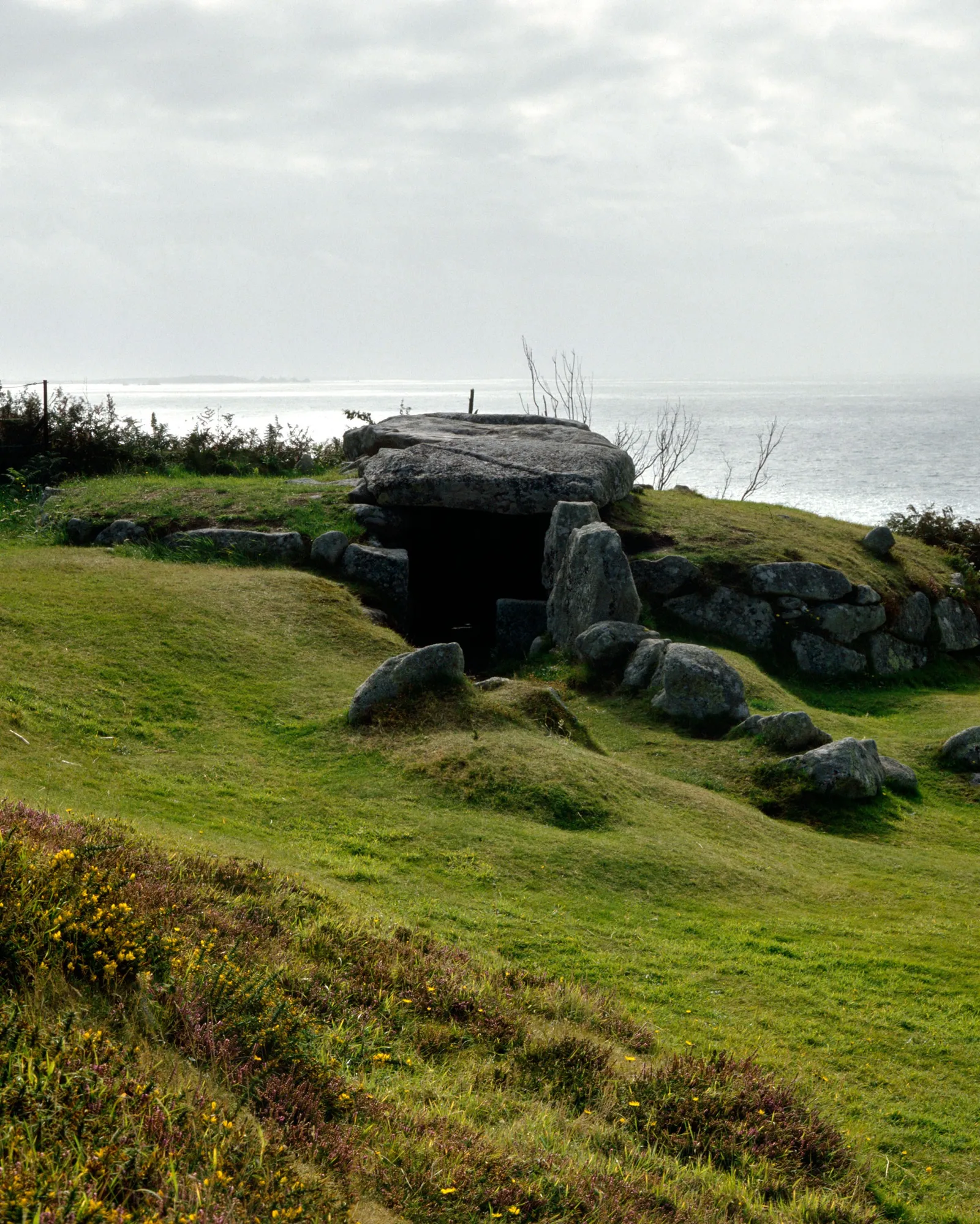 The capstone of Bant's Carn silhouetted against a silvery sea under a pale overcast sky