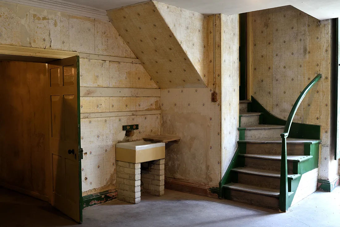 The old kitchen with its stone sink, patterned wallpaper and green-painted stair