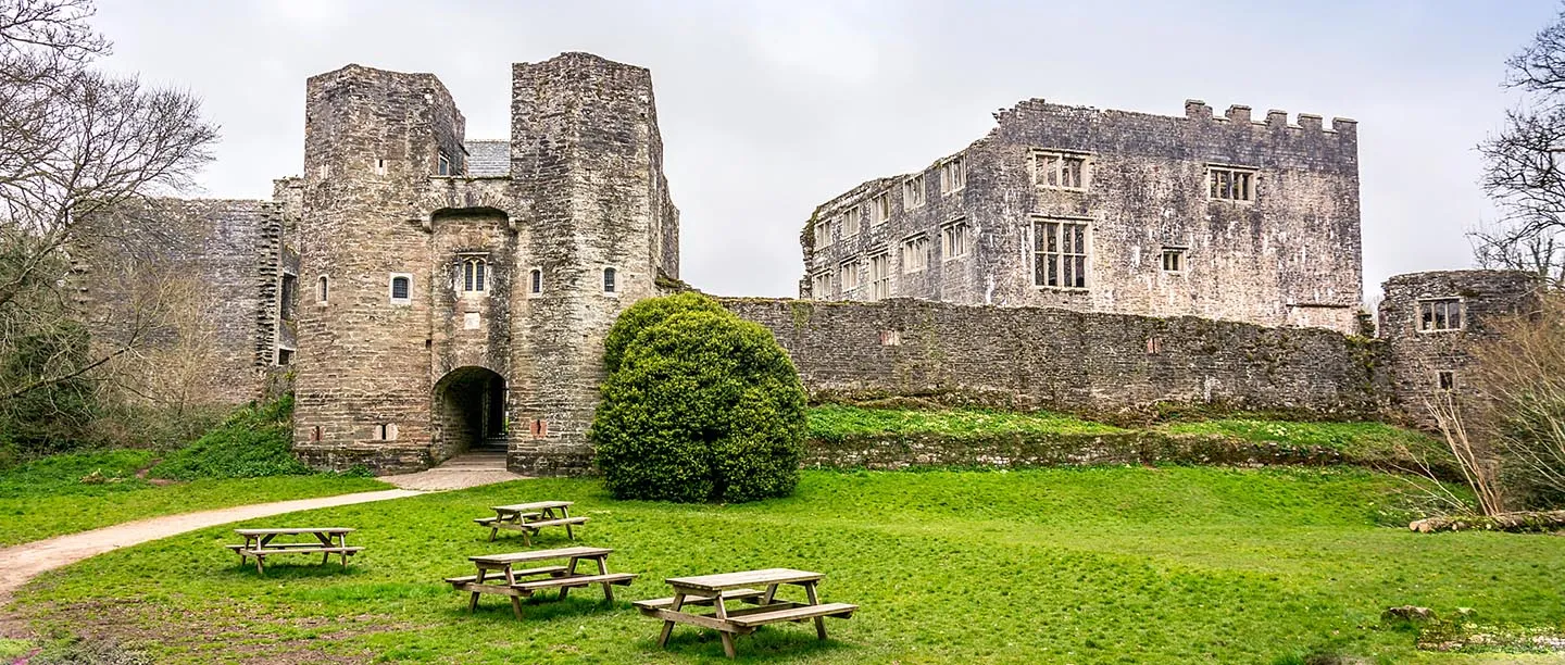 The gatehouse and curtain wall above a lawn with picnic tables, with the mansion behind