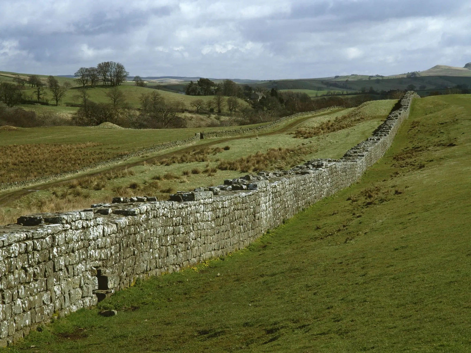 A long stretch of Hadrian's Wall crossing green fields near Birdoswald under a cloudy sky