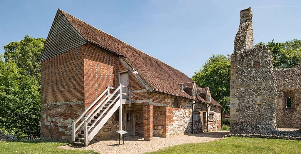 The brick and stone farmhouse at Bishop's Waltham Palace with a wooden outside stair and tiled roof, beside a ruined flint chimney stack