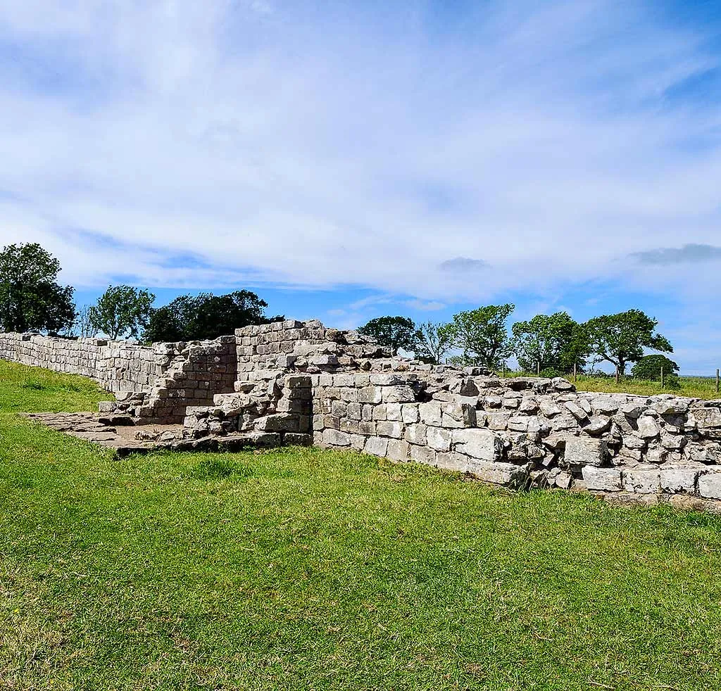 Black Carts Turret and its wing wall on Hadrian's Wall, low stone walls on green grass with trees and a blue sky