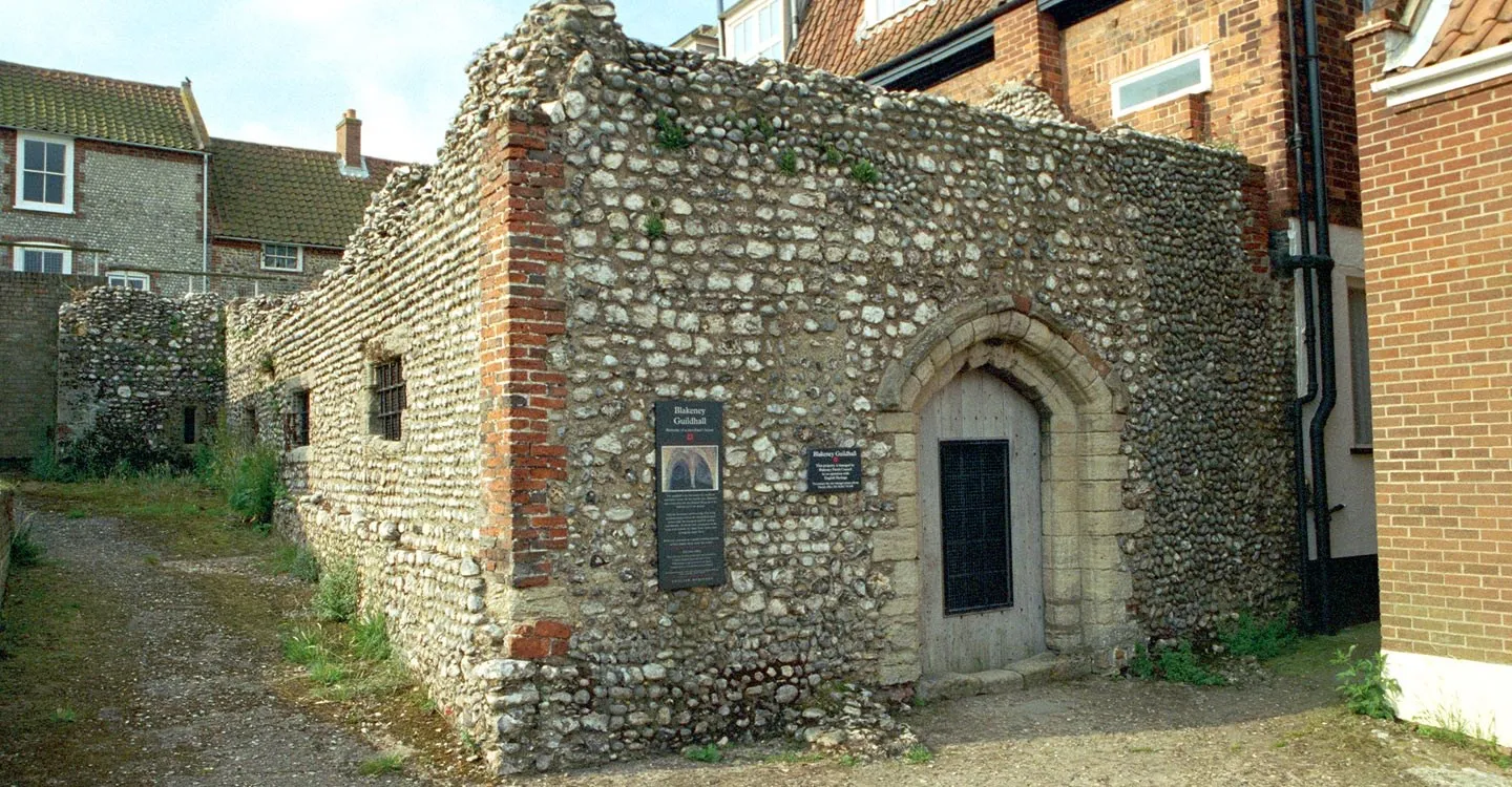Blakeney Guildhall's flint walls with brick quoins and a pointed stone doorway, between village houses