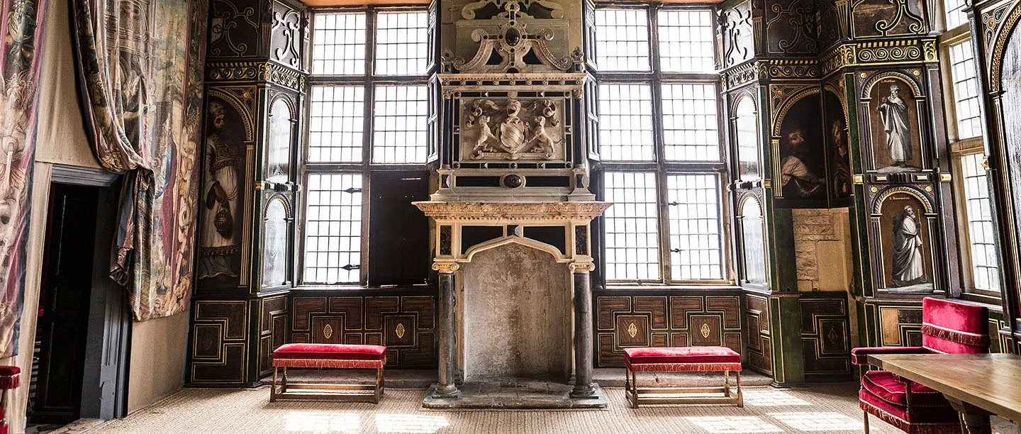 A Little Castle room with painted panelling, a carved chimneypiece and red benches