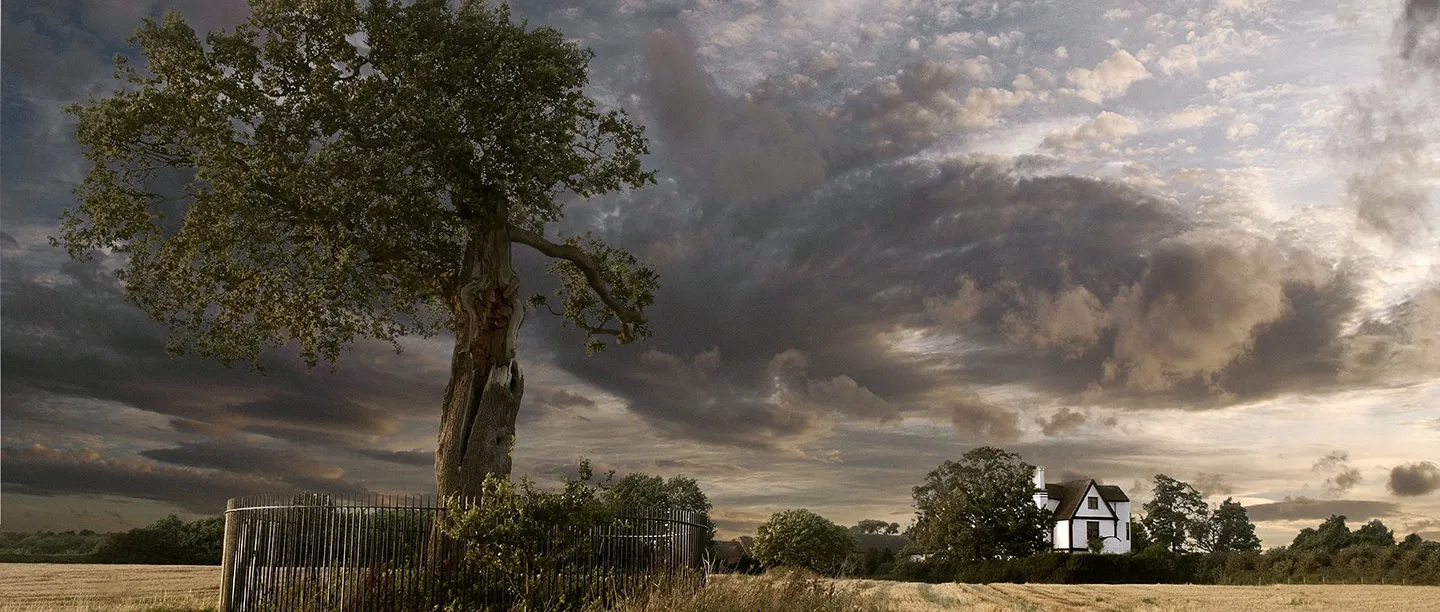 The Royal Oak inside its railings under a storm sky, with Boscobel House across the cornfield