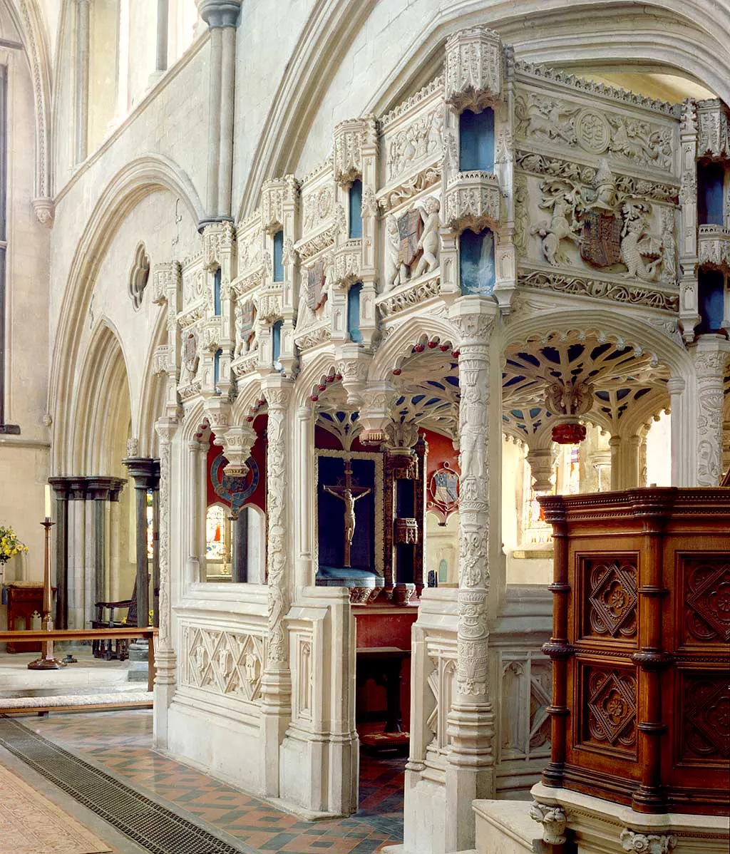 The richly carved white stone De La Warr chantry chapel inside Boxgrove Priory church, with heraldic shields, fan vaulting and an oak pulpit