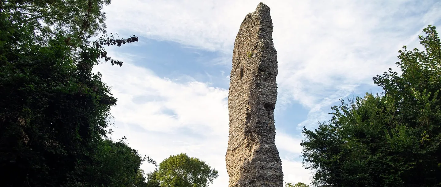 The tall, narrow surviving wall of Bramber Castle's gatehouse tower rising beside trees against a blue sky
