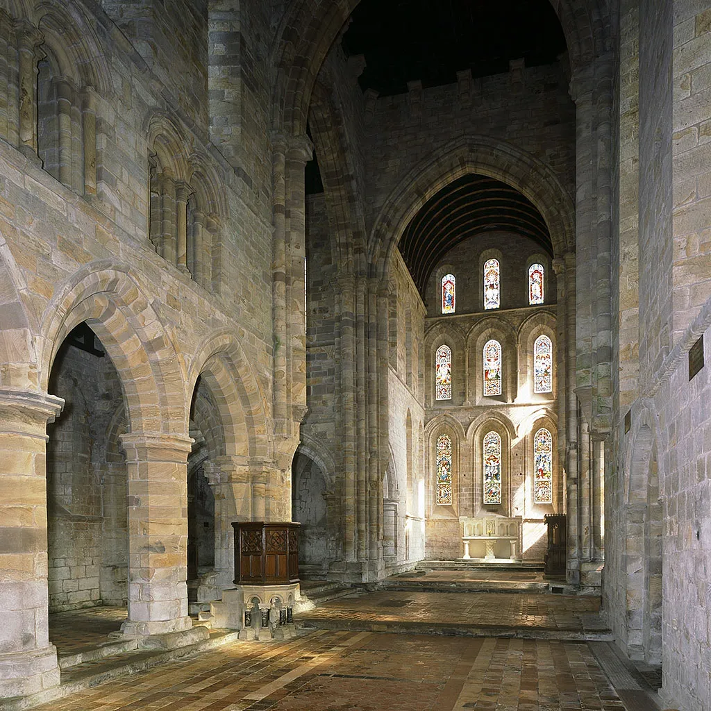 The nave of Brinkburn Priory church looking east past sandstone arches and a wooden pulpit to the altar and stained glass
