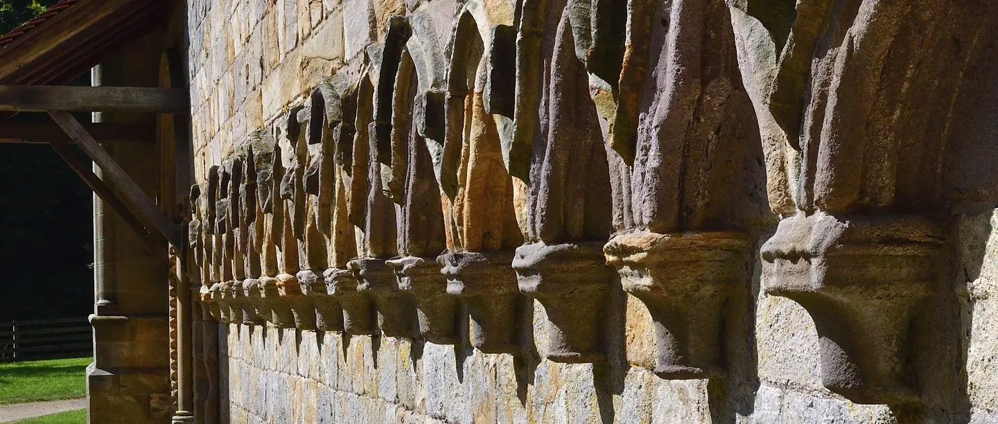 A long row of weathered carved corbels along the sandstone wall of Brinkburn Priory, catching low sunlight