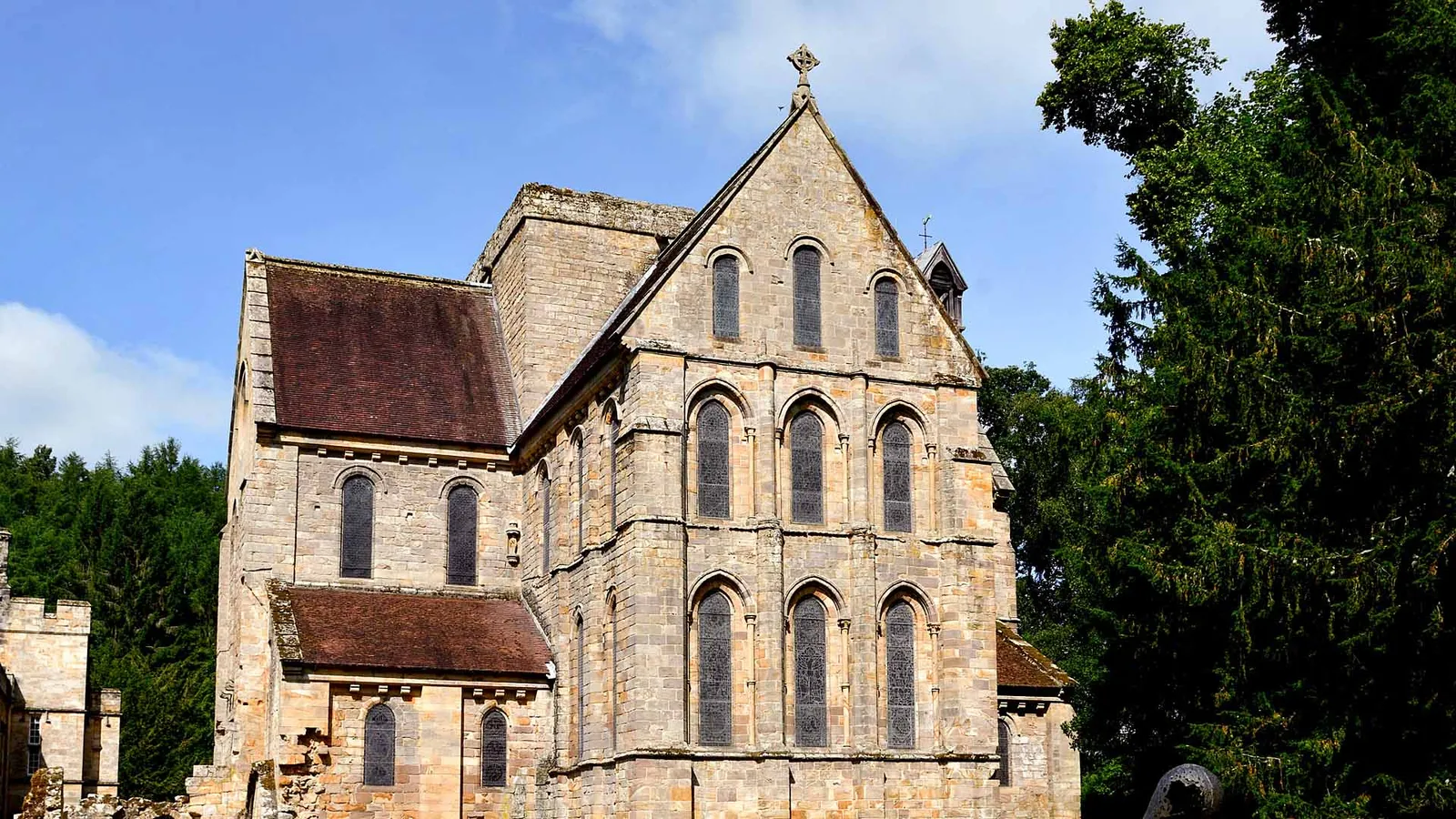 The tall gabled east end of Brinkburn Priory church with rows of round-headed lancet windows, framed by dark yew trees