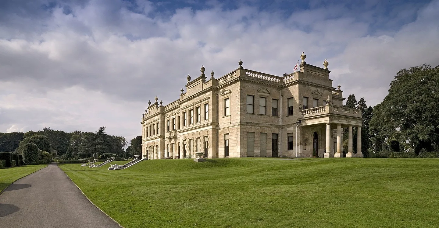 The hall's long Italianate front above sloping lawns, with greyhound statues on the terrace steps