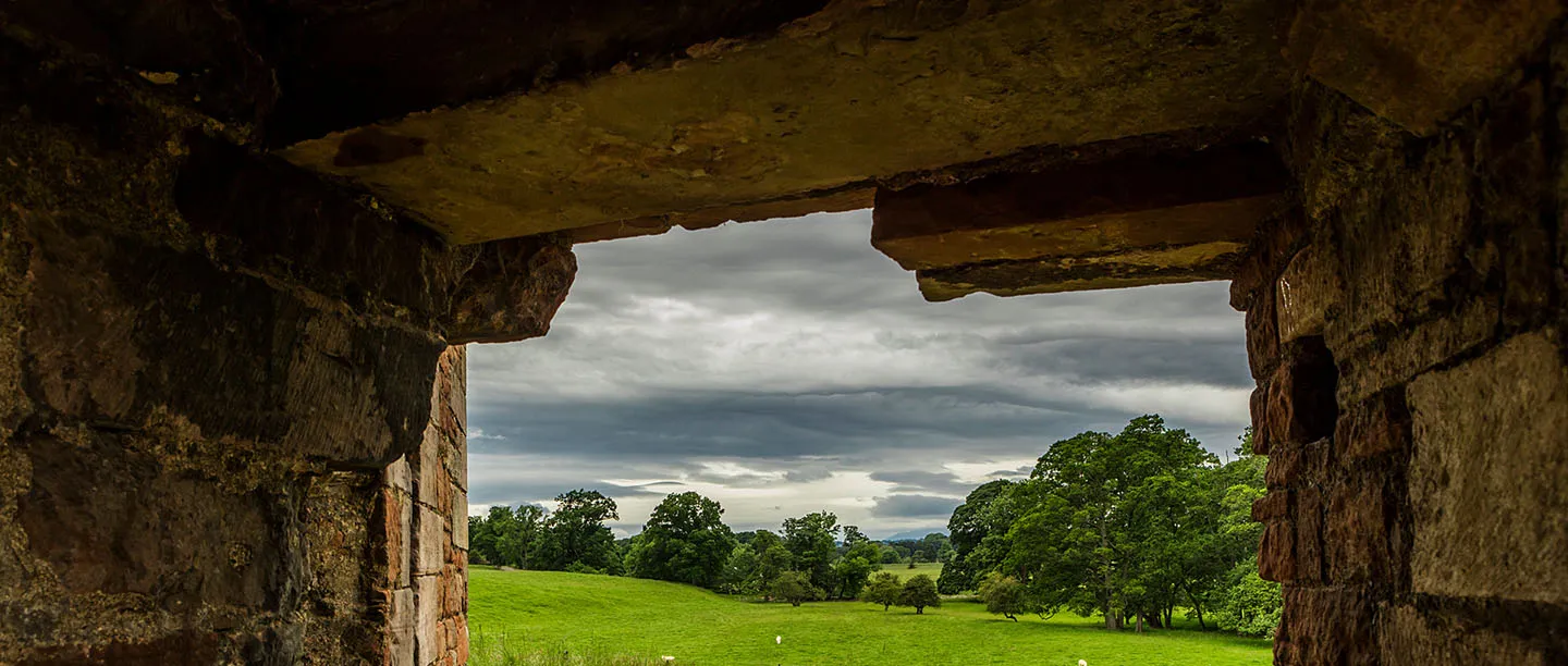 Parkland and trees seen through a doorway in the castle's thick sandstone walls