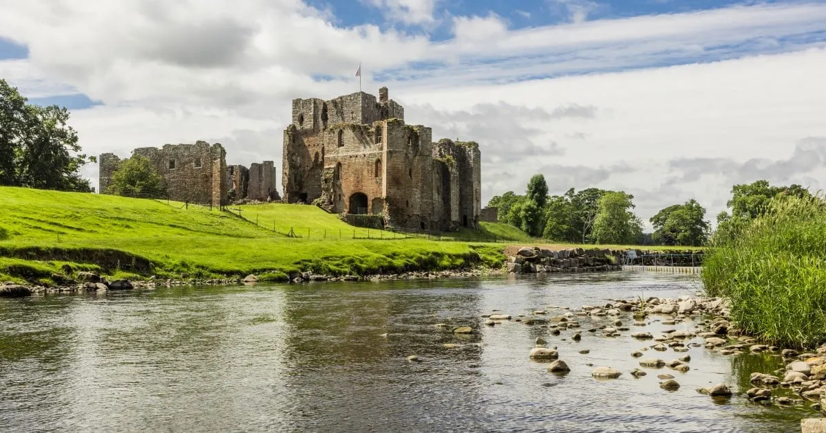 Brougham Castle's keep and ruined ranges on a green bank above the River Eamont