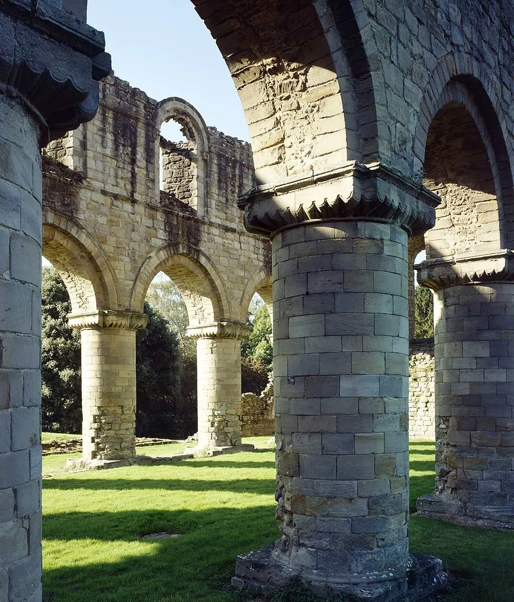 Massive round stone piers and arches in the ruined nave of Buildwas Abbey, casting shadows across the sunlit grass