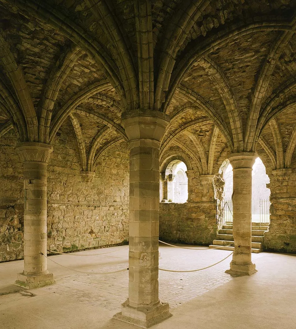 The rib-vaulted chapter house of Buildwas Abbey, with slender piers, a rope barrier and steps up to an arched doorway