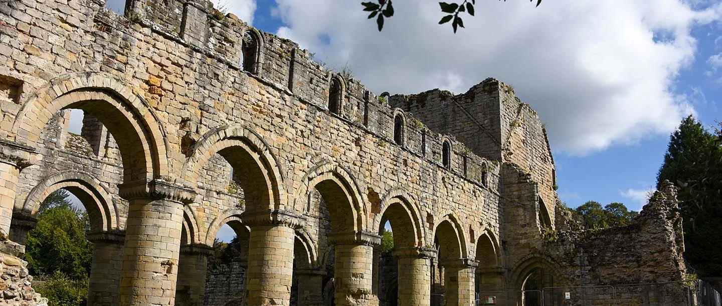 The arcade of round arches on stout cylindrical piers in the nave of Buildwas Abbey, against a blue sky with white clouds