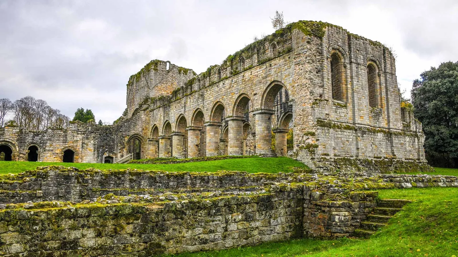 The roofless nave of Buildwas Abbey with its round Norman arches and crossing tower, above moss-covered wall footings and a lawn