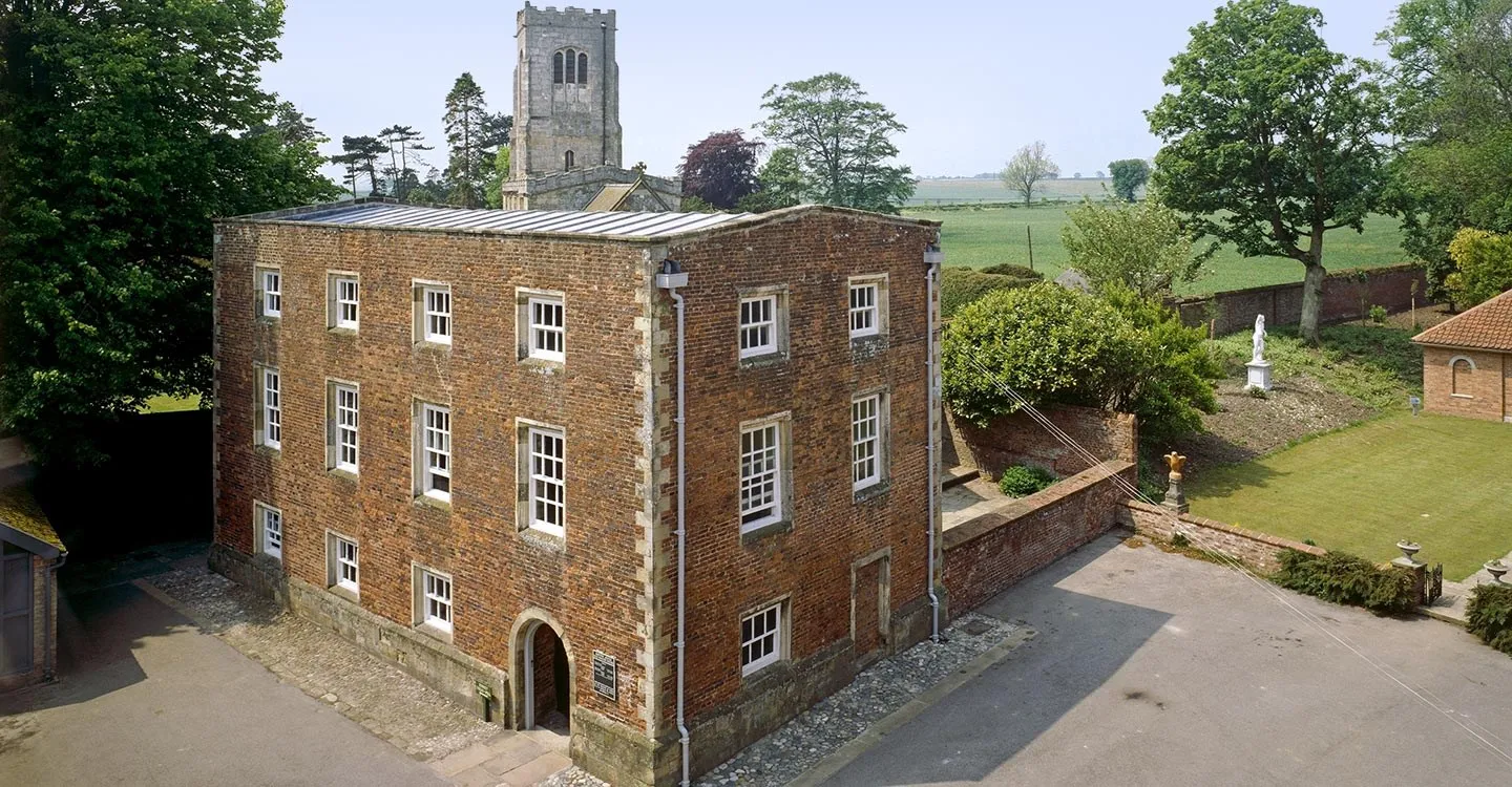 The red-brick casing of Burton Agnes Manor House seen from above, with the church tower, a walled garden and fields beyond