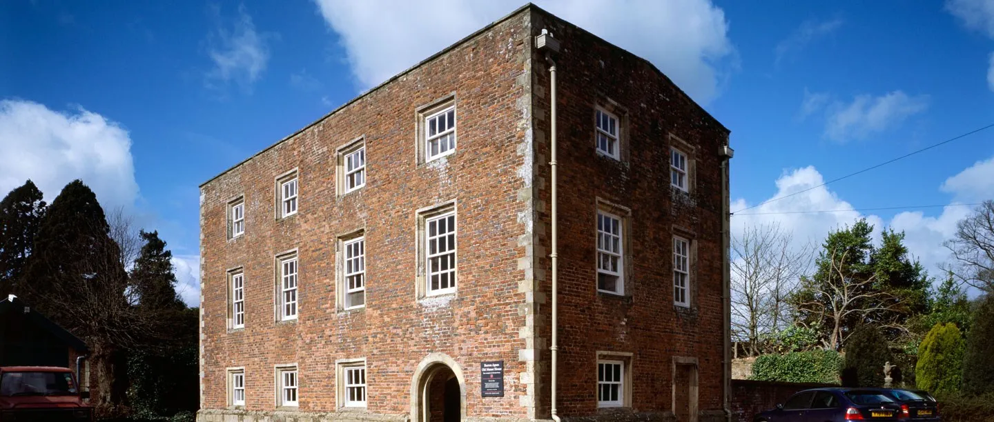 The red-brick front of Burton Agnes Manor House with sash windows and an arched doorway under a blue spring sky