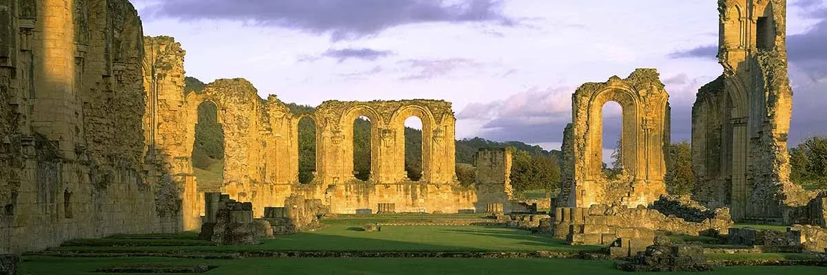 The ruined arches of Byland Abbey's church glowing in evening sun, with grass between the pier bases