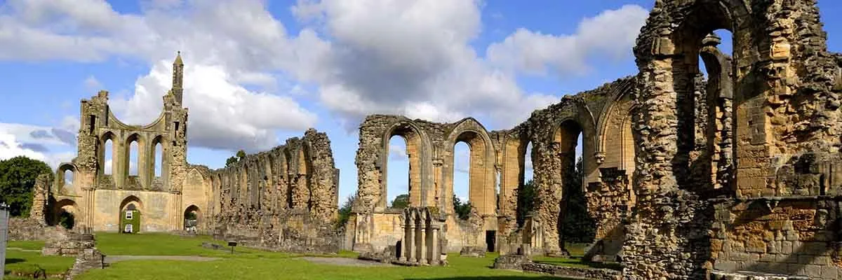 The west front of Byland Abbey with its half rose window and the long nave wall under a cloudy sky
