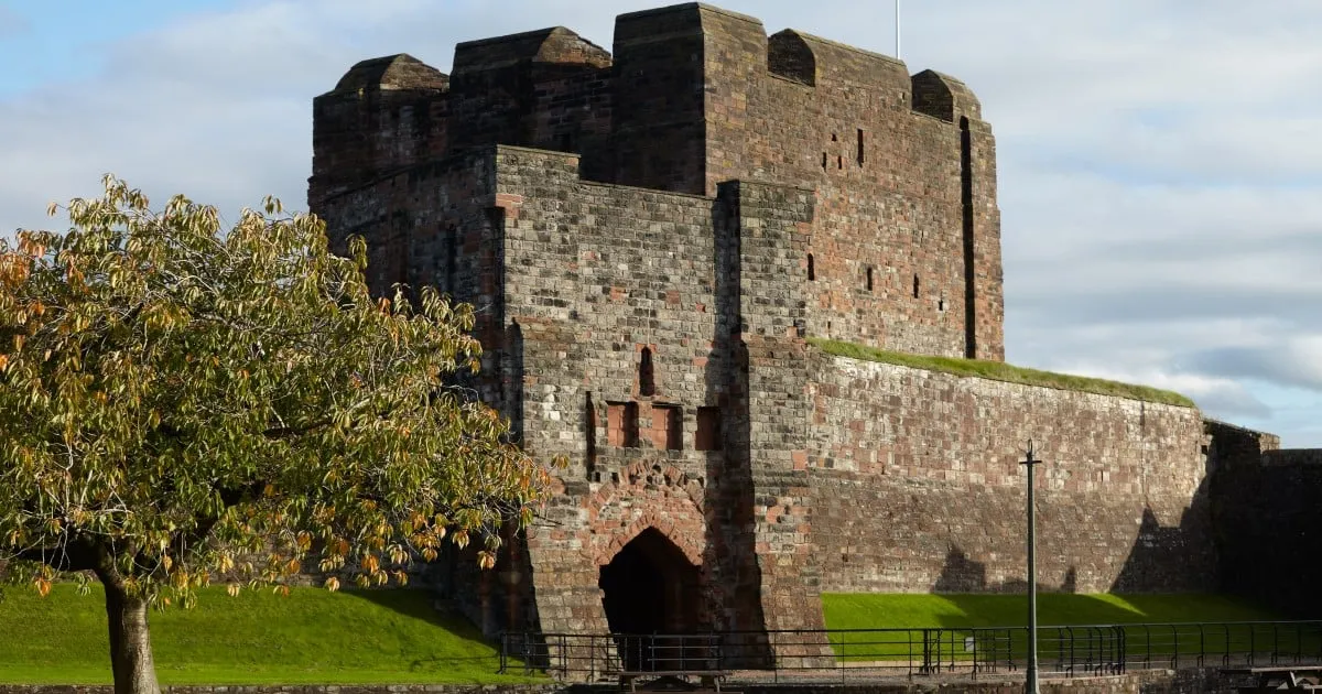 The keep and outer gatehouse in autumn sun behind a tree turning gold