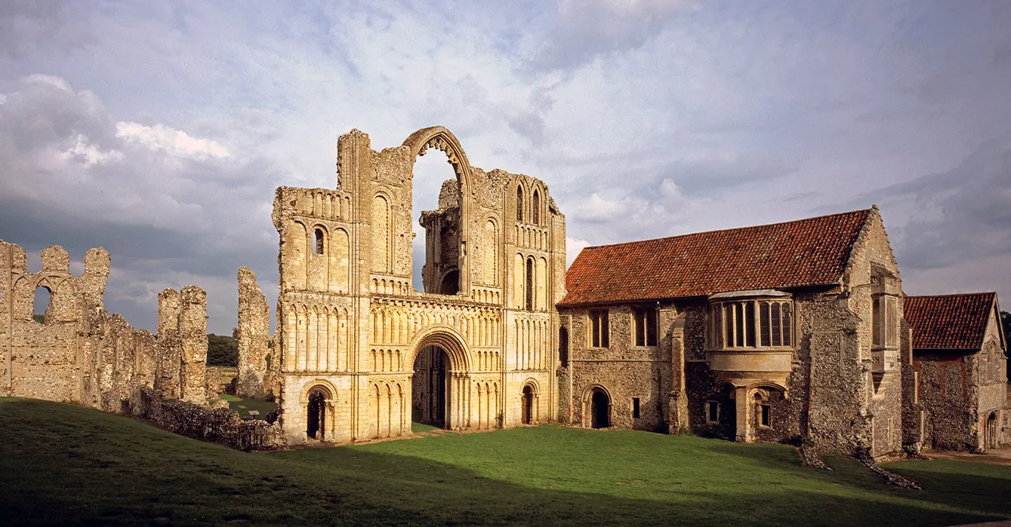 The ornate Norman west front of Castle Acre Priory church beside the prior's lodging in warm evening light