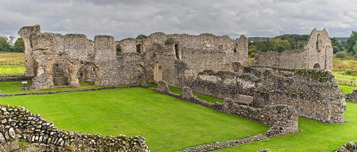 The flint walls of the priory's cloister ranges around a green lawn under a cloudy sky