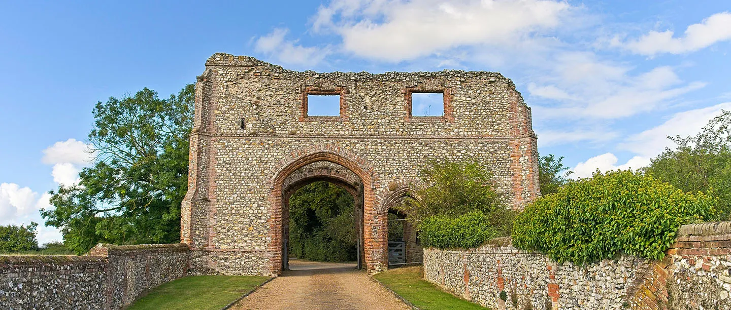 The flint and brick priory gatehouse with its arched entrance and a gravel drive