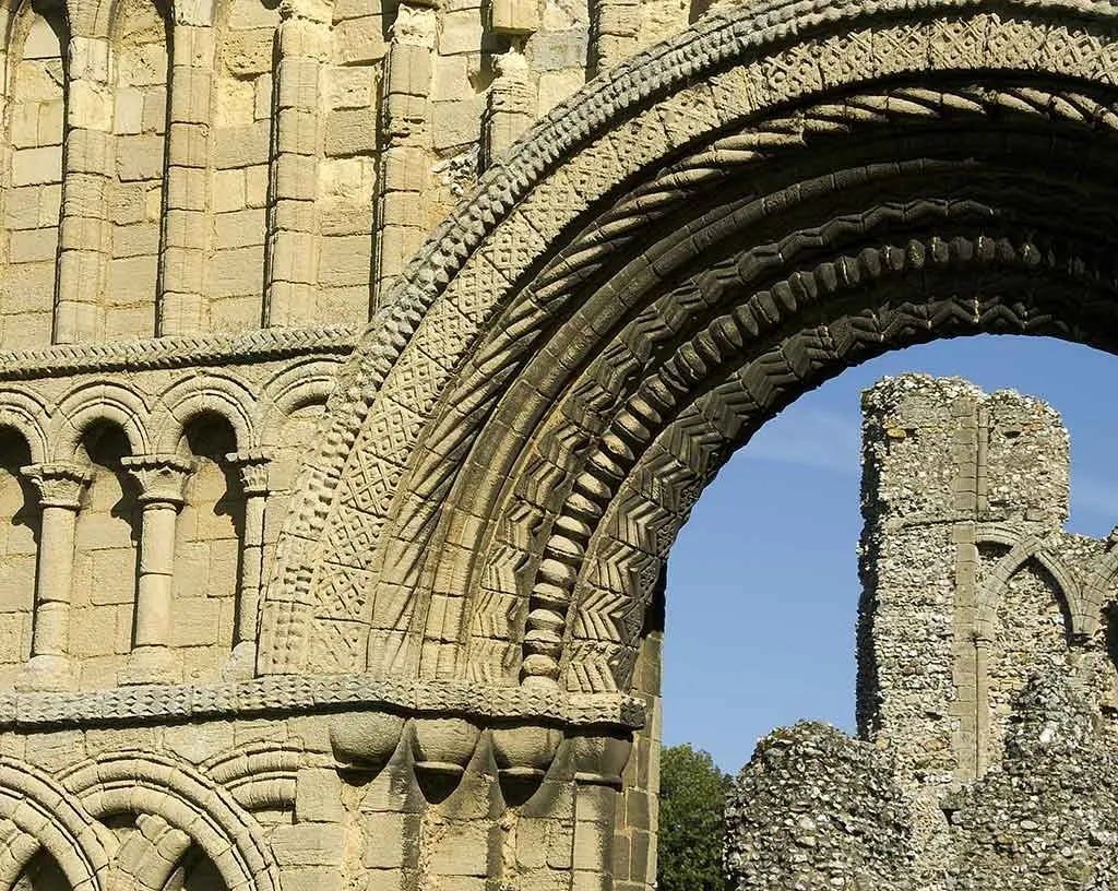 Carved chevron and zigzag mouldings of the west doorway framing a ruined flint tower