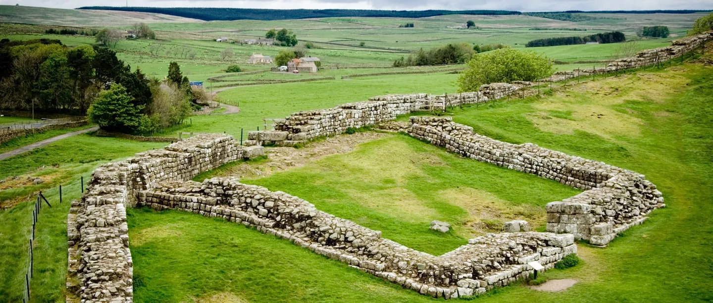 The stone walls of Milecastle 42 on Hadrian's Wall at Cawfields, with stone farmhouses and fields beyond