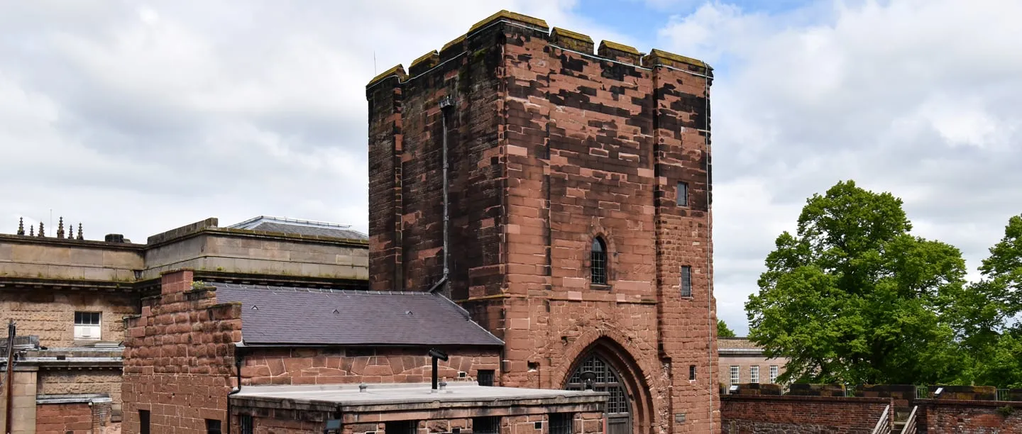 The square red sandstone Agricola Tower at Chester Castle with a pointed arched doorway, beside lower buildings and a battlemented wall