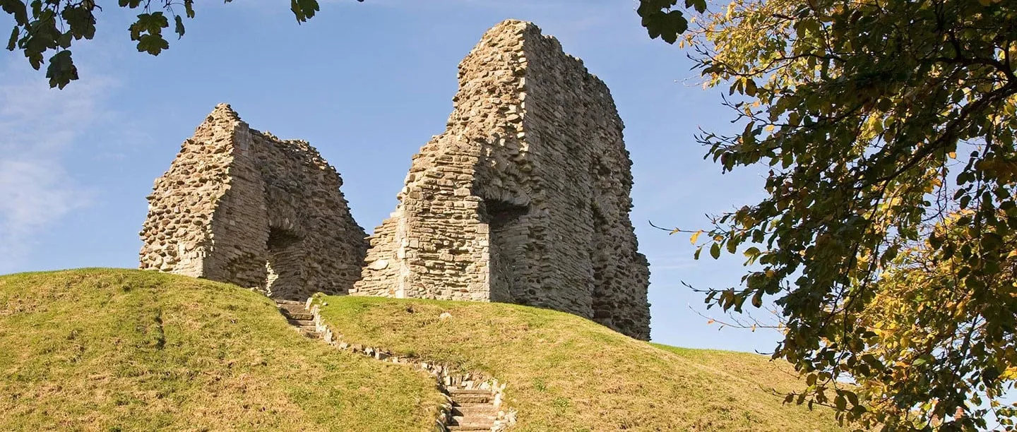 The ruined keep of Christchurch Castle on its grassy motte, with stone steps and an autumn tree