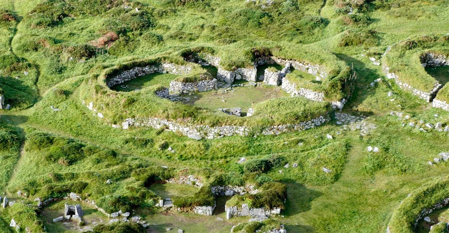 An aerial view of a courtyard house at Chysauster, its rooms of dry-stone walls set into grassy banks around a central courtyard