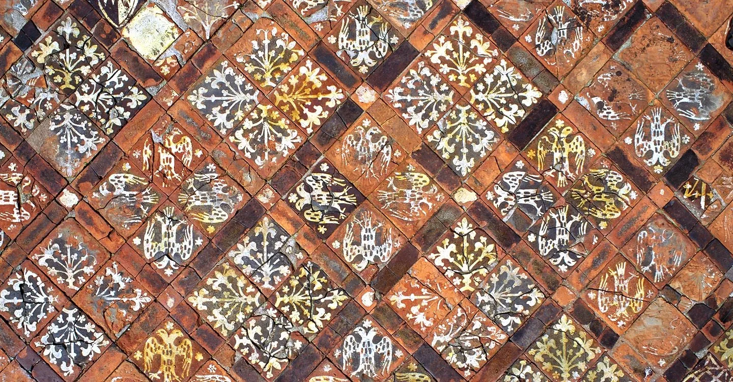 Medieval floor tiles at Cleeve Abbey decorated with heraldic eagles and stylised plants in cream on red clay