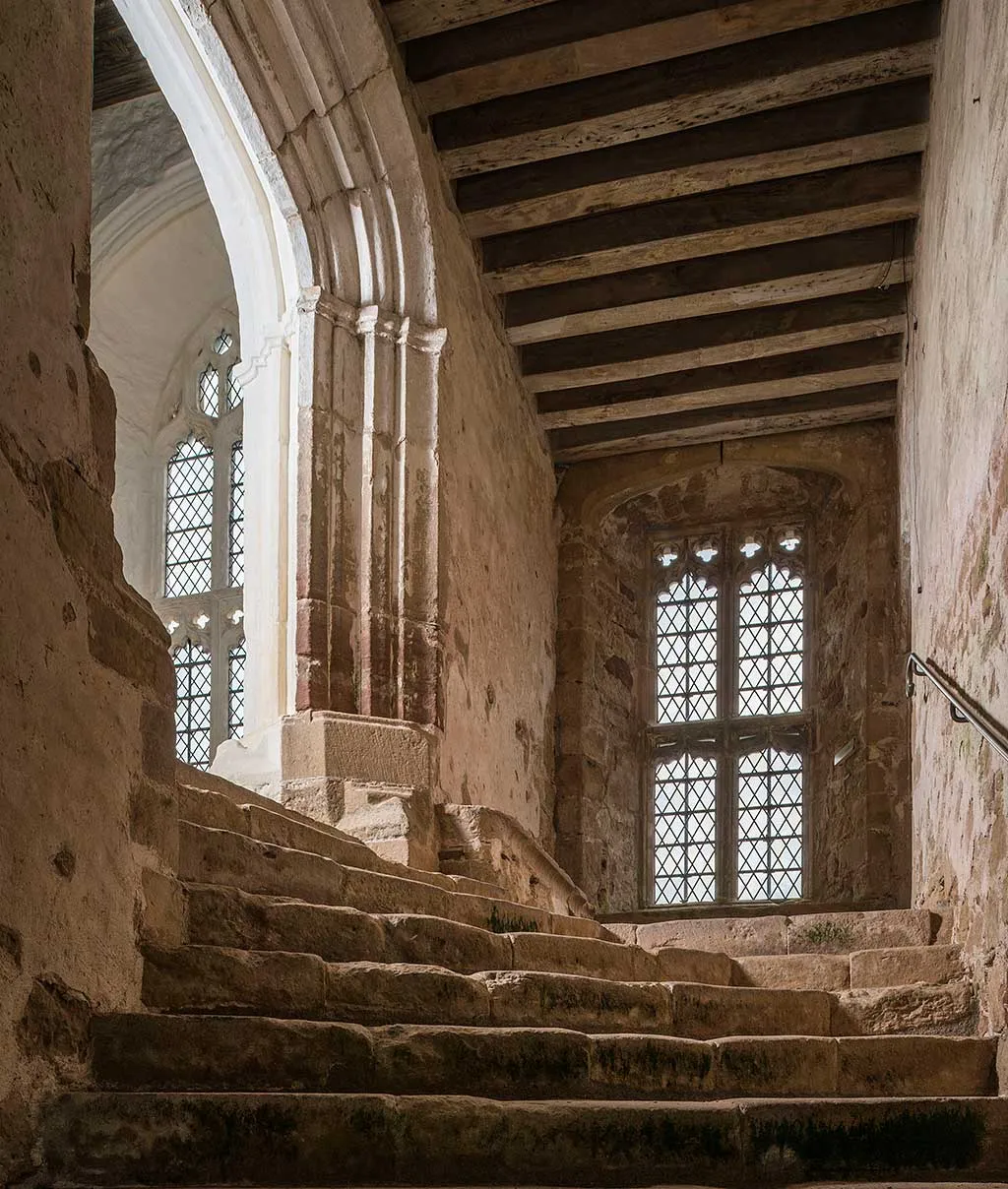 Worn stone steps rising to the refectory at Cleeve Abbey under a beamed ceiling, lit by leaded windows