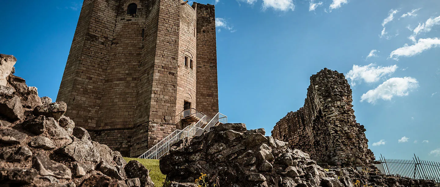 The great cylindrical keep and its buttresses above the rocky curtain wall under a blue sky