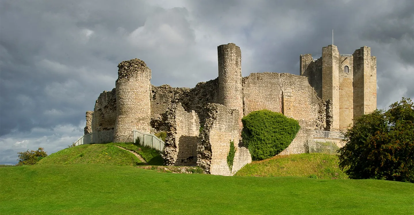 The curtain wall's round towers and the keep on their grassy mound beneath dark storm clouds